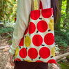 Person holding a tote bag with red and yellow circular patterns in a forest setting