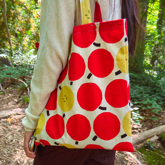 Person holding a tote bag with red and yellow circular patterns in a forest setting
