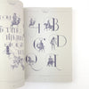 Open book with decorative lettering and illustrations on a white background