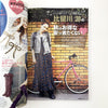 Magazine layout with a woman in a patterned dress standing next to a pink bicycle against a brick wall.